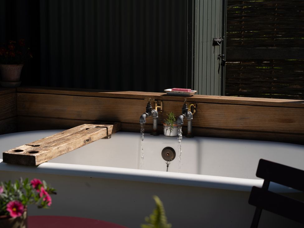A bathtub with faucets and a wooden plank at Hurdlemakers Hut in Piddletrenthide