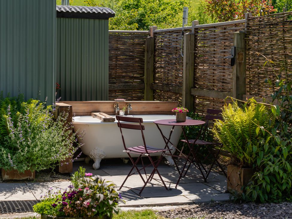 A garden setup with a bathtub and a table with chairs at Hurdlemakers Hut in Piddletrenthide