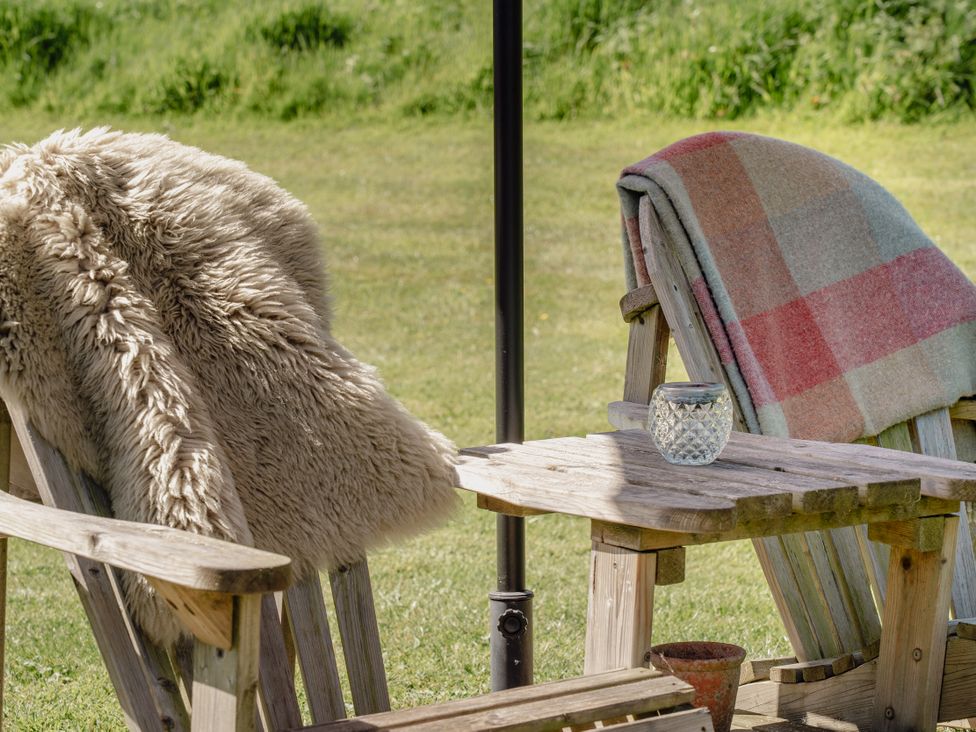 A chair with a blanket and a table in an outdoor seating area at Hurdlemakers Hut in Piddletrenthide