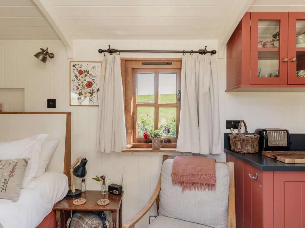 A bedroom with a window, chair, and kitchen cabinet at Spindleberry Hut in Piddletrenthide