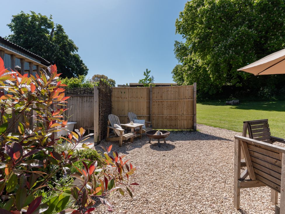 A garden with wooden chairs, a table, and a fire pit at Spindleberry Hut in Piddletrenthide