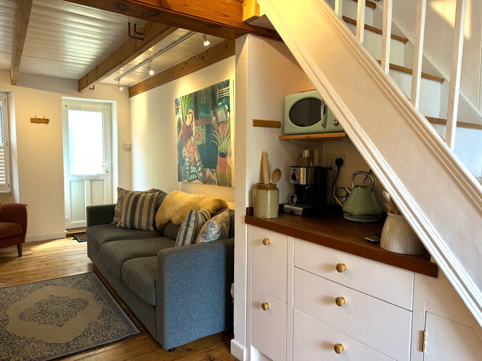 A living room with a gray sofa striped pillows wall art and kitchen appliances under stairs at Bodillys Cottage in Newlyn