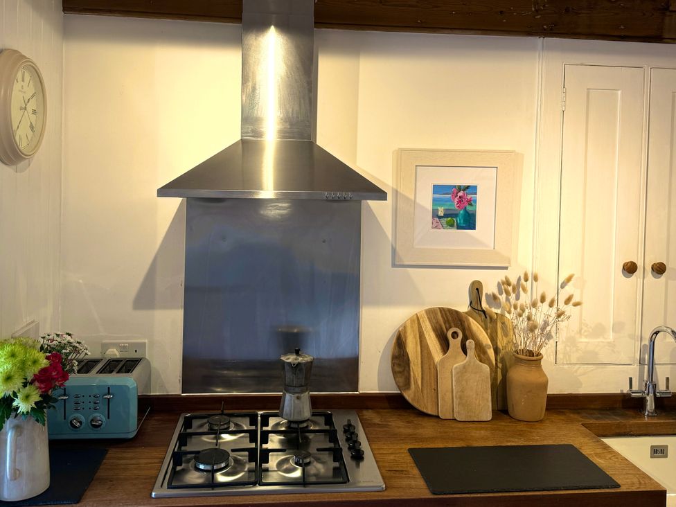 A kitchen counter with a gas stove coffee maker toaster flowers wooden cutting boards and a vase with dried plants at Bodillys Cottage in Newlyn