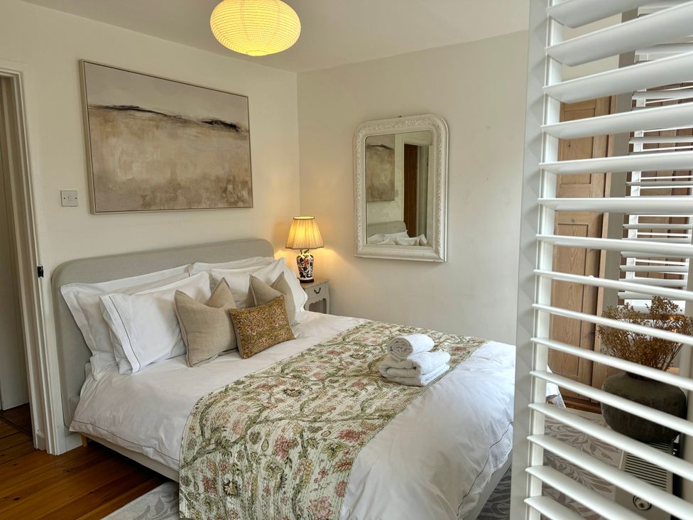 A bedroom with a bed, pillows, a bedside table with a lamp and a wall mirror at Bodillys Cottage in Newlyn