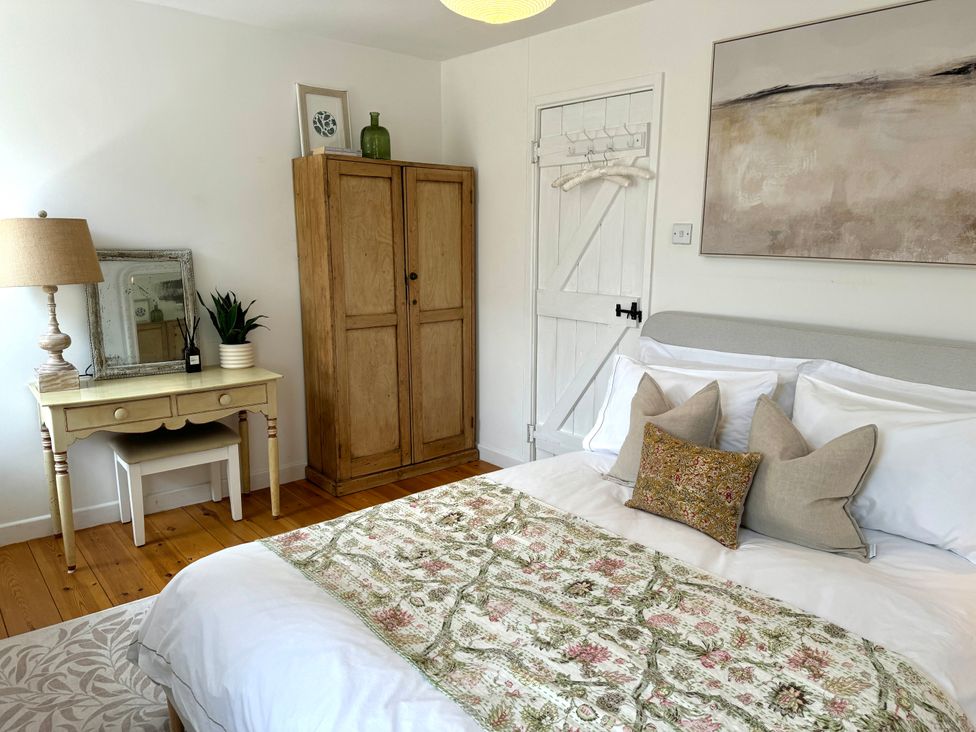 A bedroom with a bed a wooden wardrobe a desk with a lamp and plant and a door with hangers at Bodillys Cottage in Newlyn