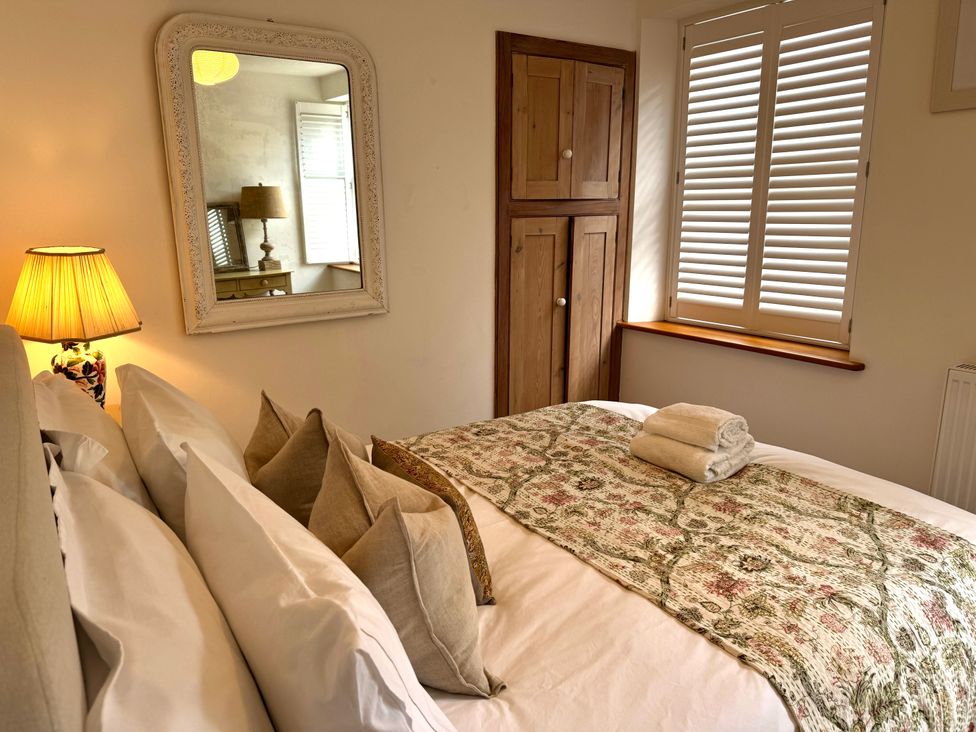A bedroom with a bed pillows lamp wooden cupboard and window shutters at Bodillys Cottage in Newlyn