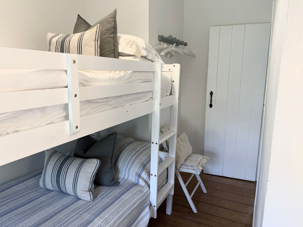 A bedroom with a white bunk bed pillows and a small chair beside a white door at Bodillys Cottage in Newlyn