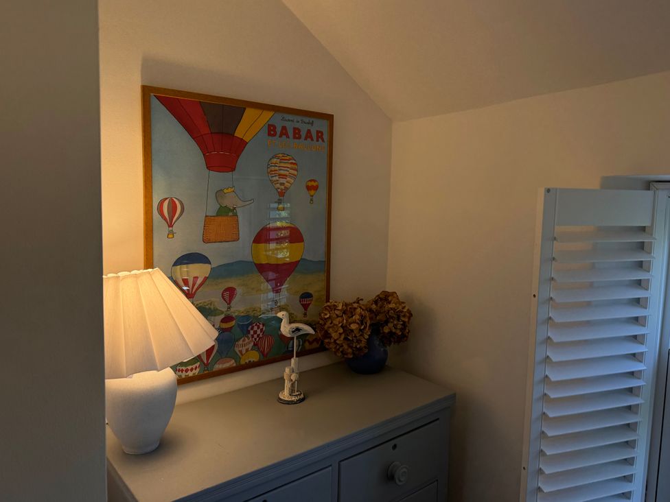 A gray cabinet with a lamp dried flowers and a decorative bird figurine under a framed hot air balloon poster at Bodillys Cottage in Newlyn
