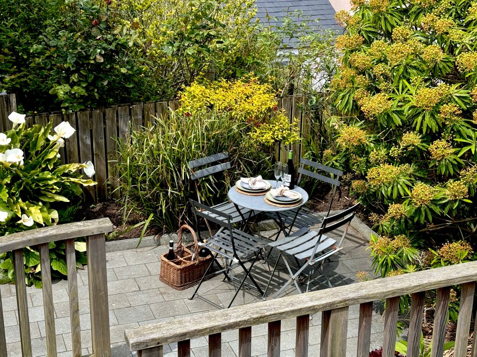 A small outdoor patio with a round table set for two surrounded by four chairs and plants at Bodillys Cottage in Newlyn
