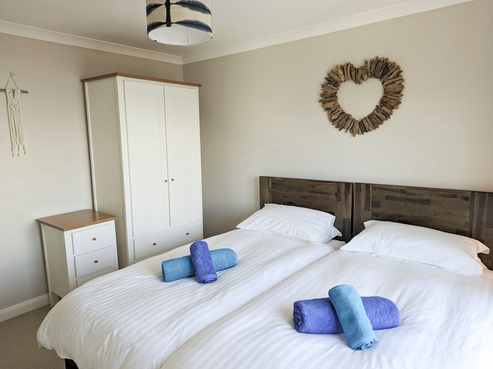A bedroom with two beds and a wardrobe at Looe Island View in Downderry