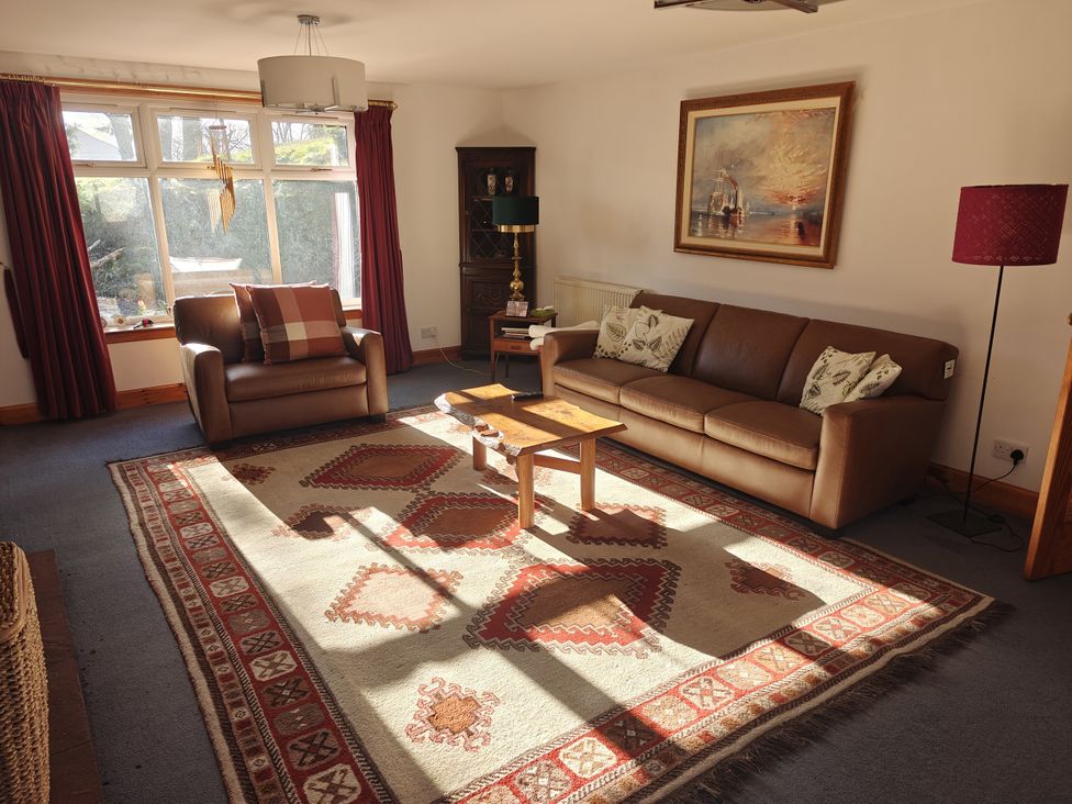 A living room with a sofa, armchair, coffee table, and rug at Ninevah in Balquhidder, Perthshire, Scotland