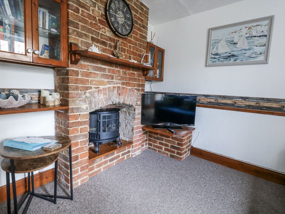 A living room with a brick fireplace and television at Saddlers Cottage in Weymouth