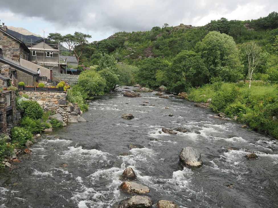 A river flowing alongside buildings and trees at Henfro in Beddgelert