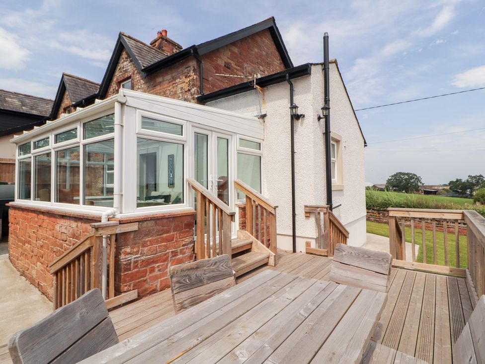 A conservatory attached to a house with a wooden deck at Rose Bank Cottage Dalston