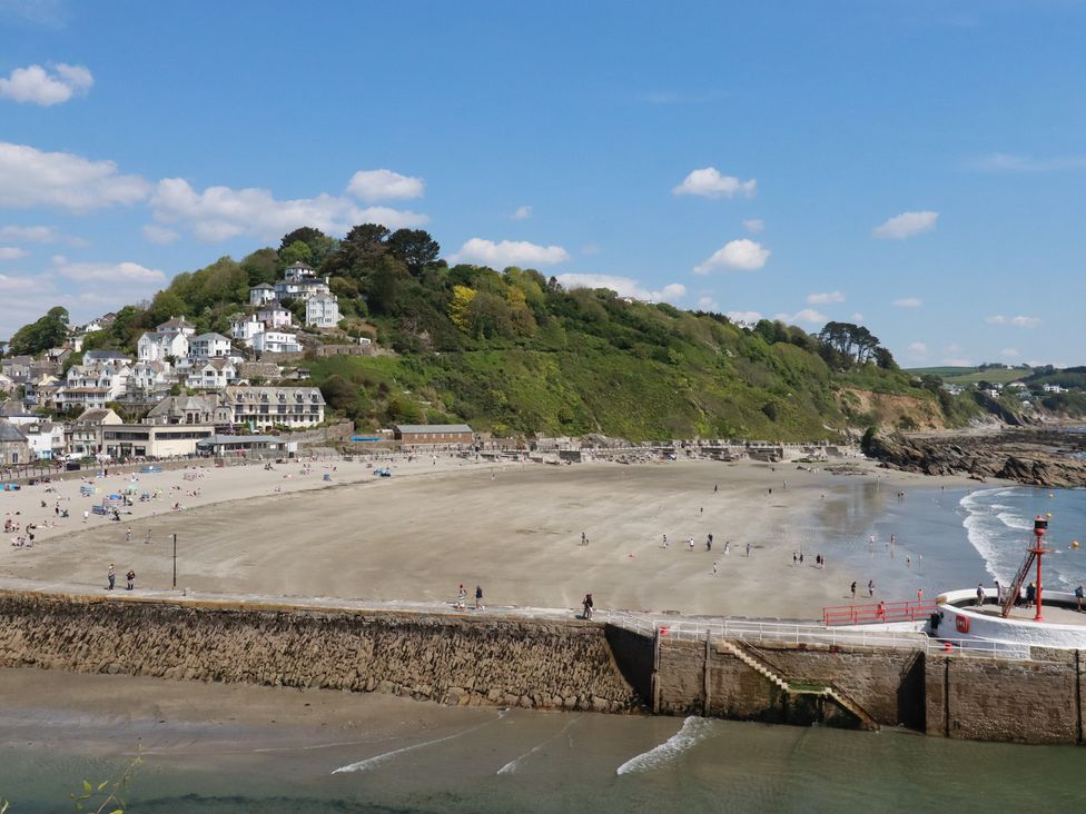 A beach with a sea wall and people walking on the sand near houses on a hillside at 3 River View in Looe