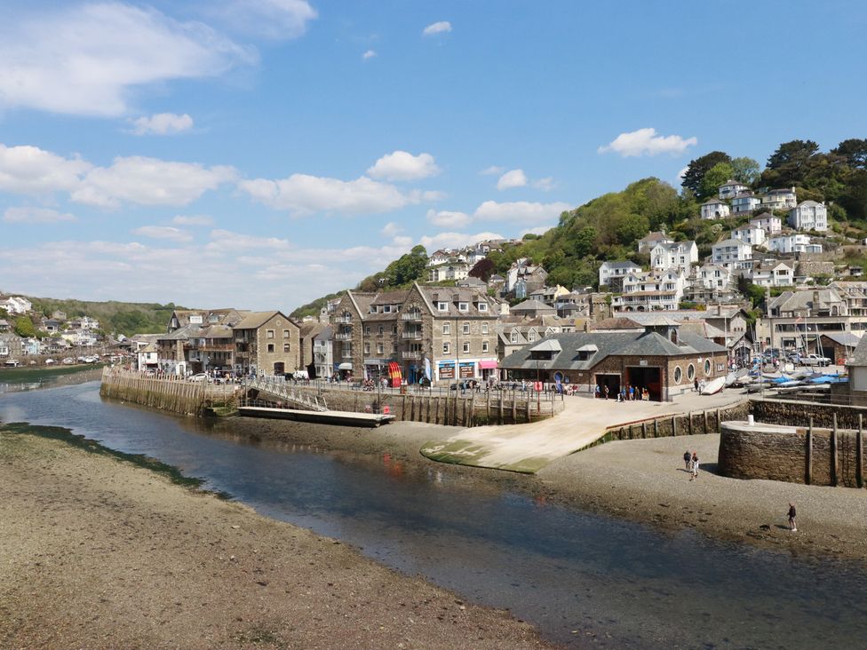 A river with a boat ramp and buildings along the shore with houses on a hill in the background at 3 River View in Looe