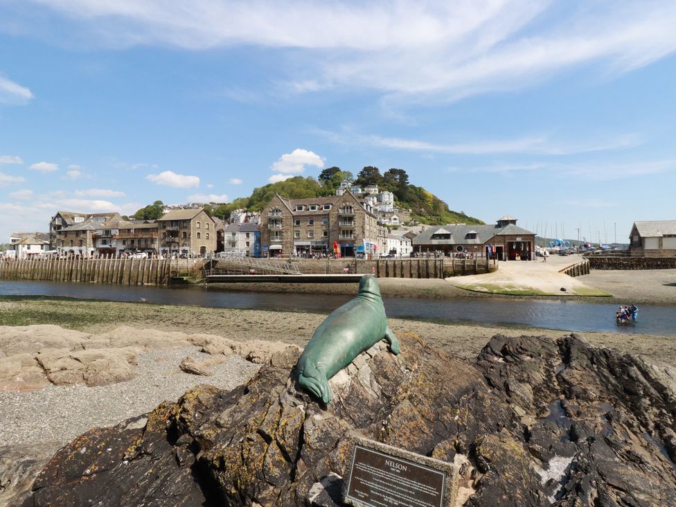 A bronze seal sculpture on rocks overlooking a river with stone buildings and green hillside in the background at 3 River View in Looe