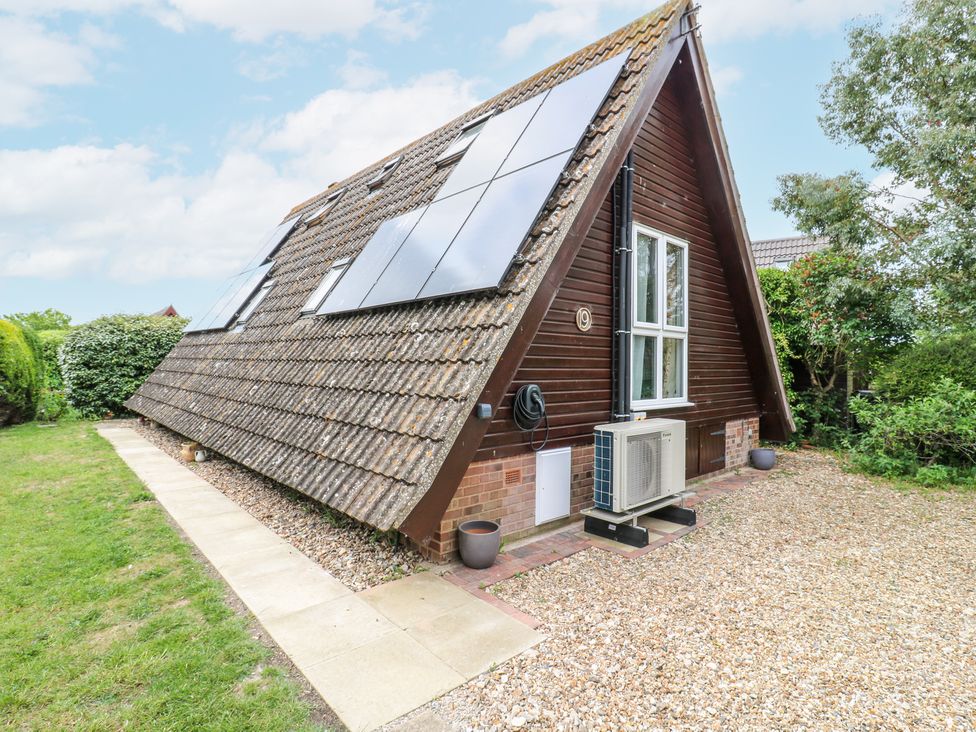 An A-frame house with solar panels on the roof a paved walkway grassy area and gravel driveway at Kingfisher in Isleham