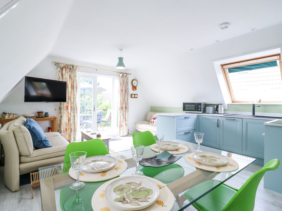 A kitchen and dining area with blue cabinets green chairs and a beige sofa at Kingfisher in Isleham