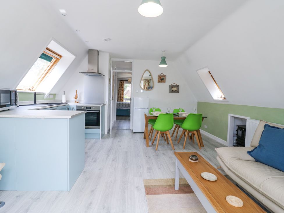 An open plan kitchen and dining area with light blue cabinets green dining chairs and a beige sofa at Kingfisher in Isleham