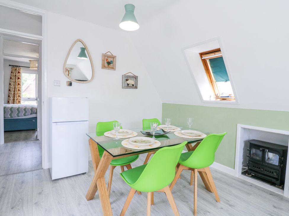 A dining room with a glass table and green chairs near a refrigerator and a small stove at Kingfisher in Isleham