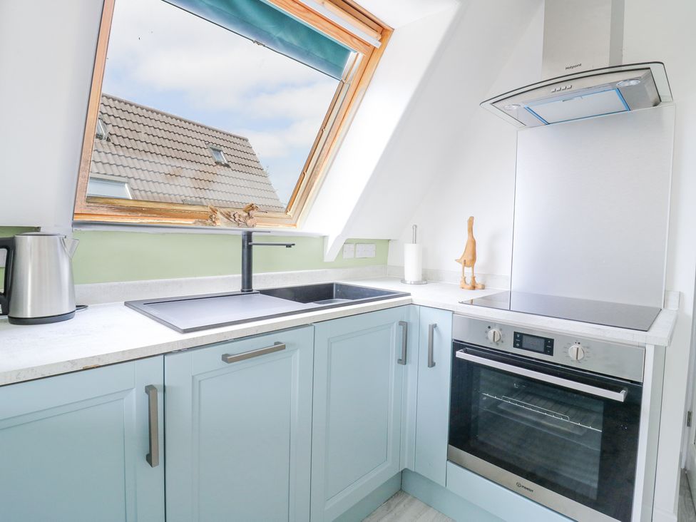 A kitchen corner with a sink under a slanted window a kettle and an oven at Kingfisher in Isleham