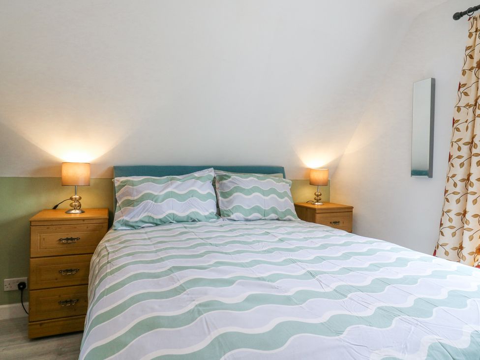 A bedroom with a bed with striped bedding two bedside tables with lamps and a curtain with leaf patterns at Kingfisher Isleham