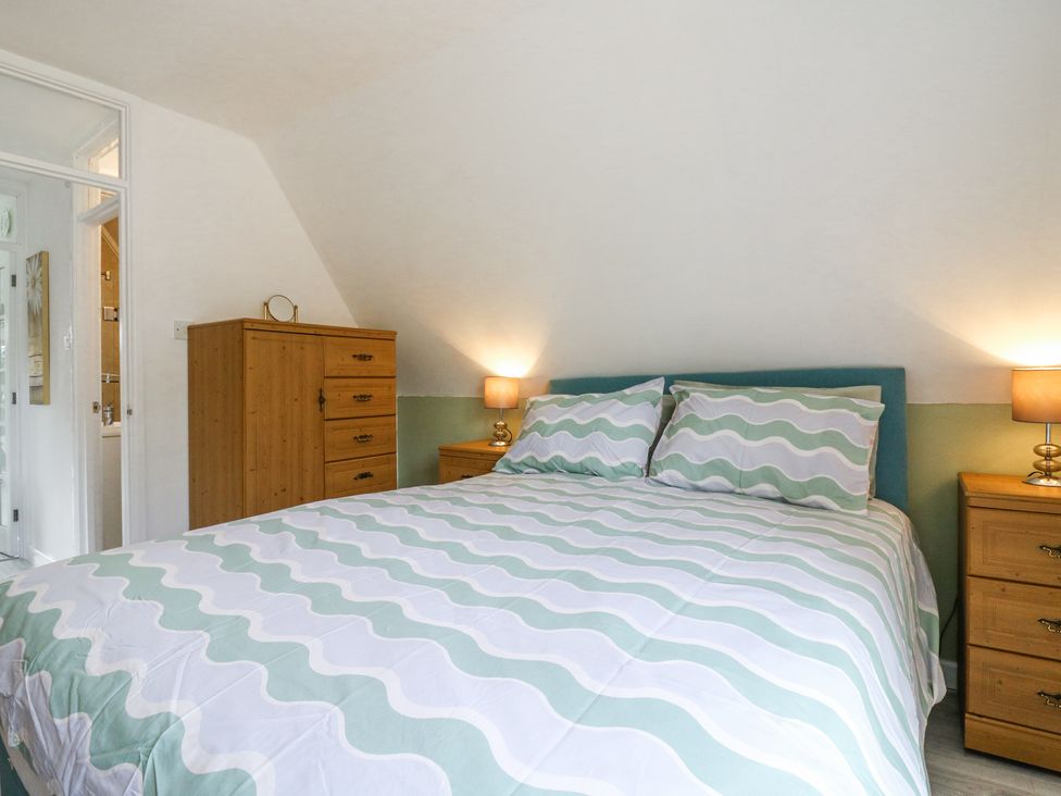 A bedroom with a bed with wavy patterned bedding two bedside tables with lamps and a wooden chest of drawers at Kingfisher in Isleham