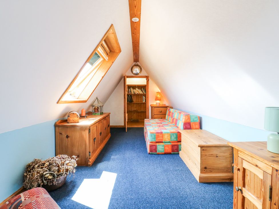 An attic room with a skylight window a wooden cabinet a colorful sofa a wooden chest and a bookshelf at Kingfisher in Isleham