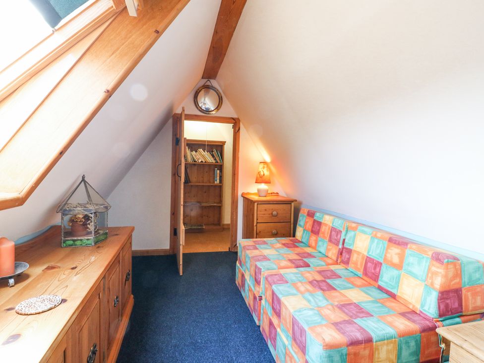 A small attic room with a multicolored checkered sofa, wooden cabinets, a lamp, and a bookshelf at Kingfisher in Isleham