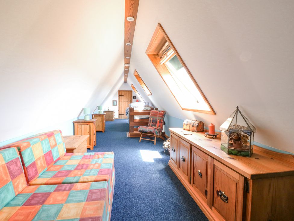 A narrow attic room with a colorful sofa, wooden cabinets, chair, bed, and skylight windows at Kingfisher in Isleham