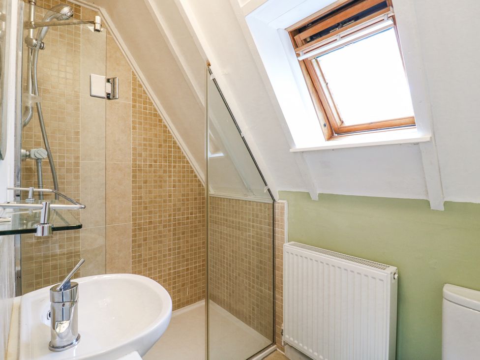 A bathroom with a sink shower area with glass door a radiator and a skylight window at Kingfisher Isleham