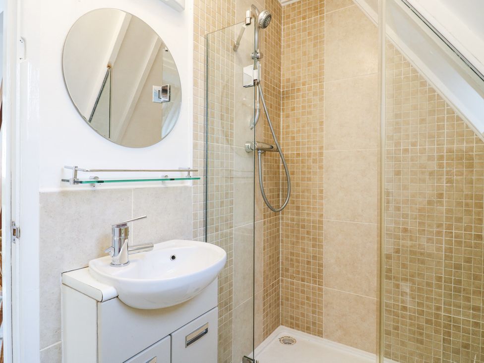 A bathroom with a white sink under a round mirror and a glass shower enclosure with beige tiled walls at Kingfisher Isleham