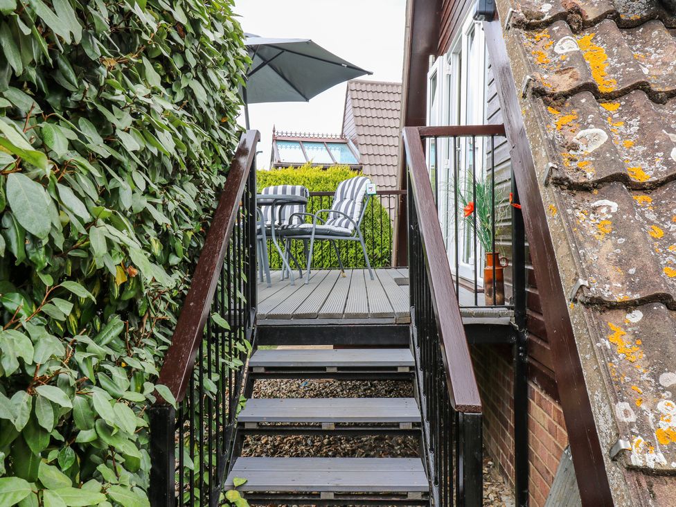 An outdoor staircase leading to a small patio with striped chairs and an umbrella near a house with a tiled roof at Kingfisher in Isleham
