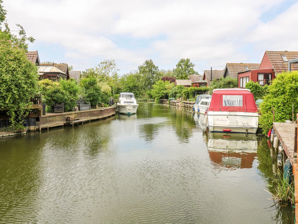 A canal with boats docked along both sides and houses with gardens along the banks at Kingfisher in Isleham