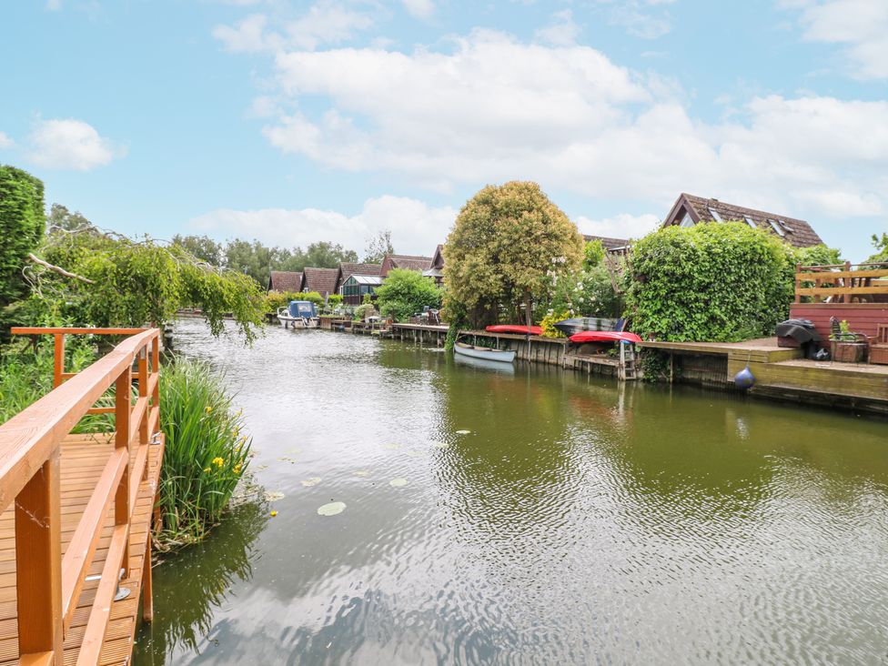 A river with boats and houses along the banks and a wooden walkway at Kingfisher in Isleham