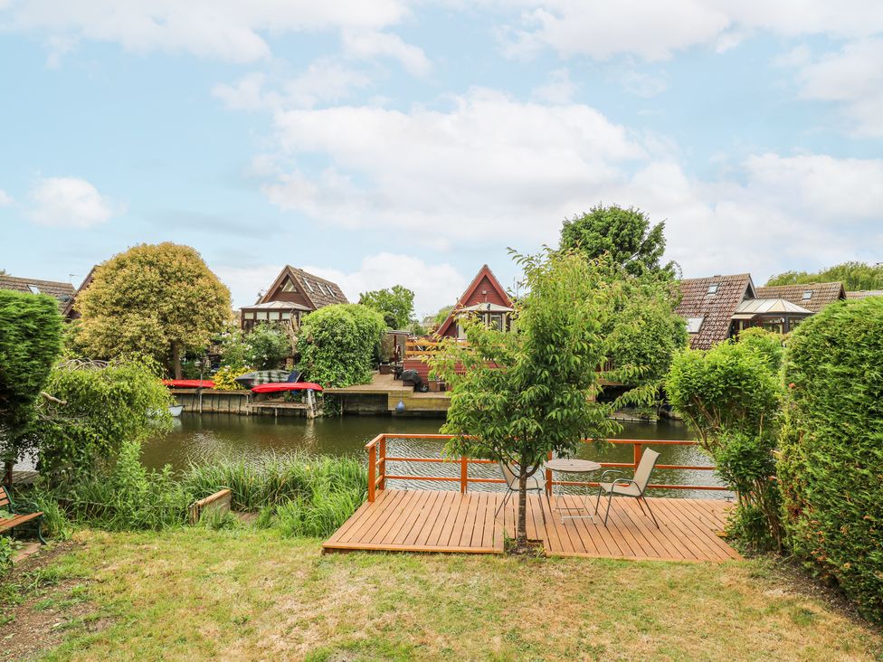 A backyard with a wooden deck overlooking a river with houses on the opposite bank at Kingfisher in Isleham