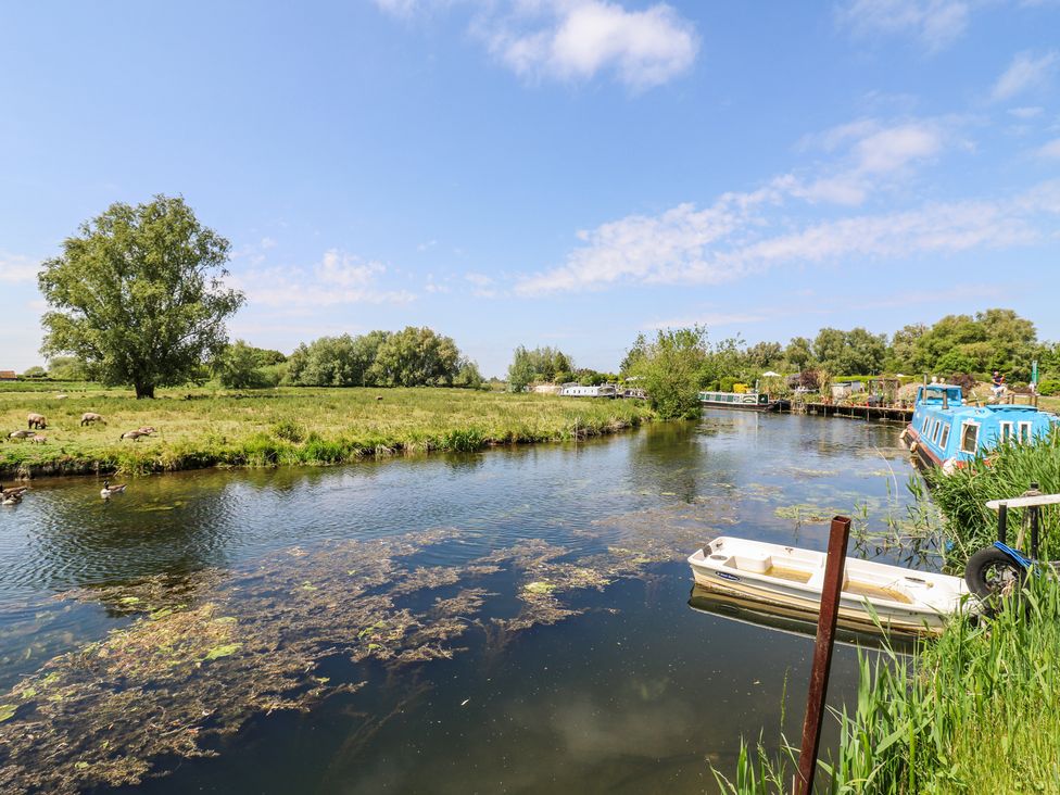 A river with boats docked along the bank and sheep grazing on grass in the field at Kingfisher in Isleham