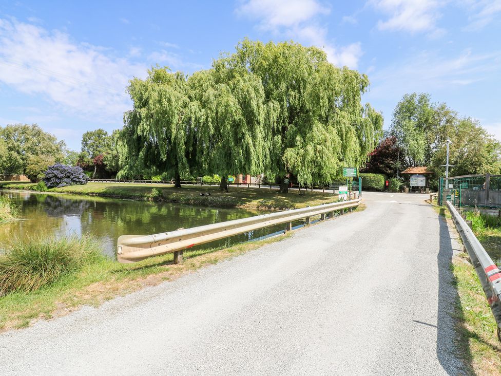 A road with guardrails crossing over water next to large trees and greenery at Kingfisher in Isleham