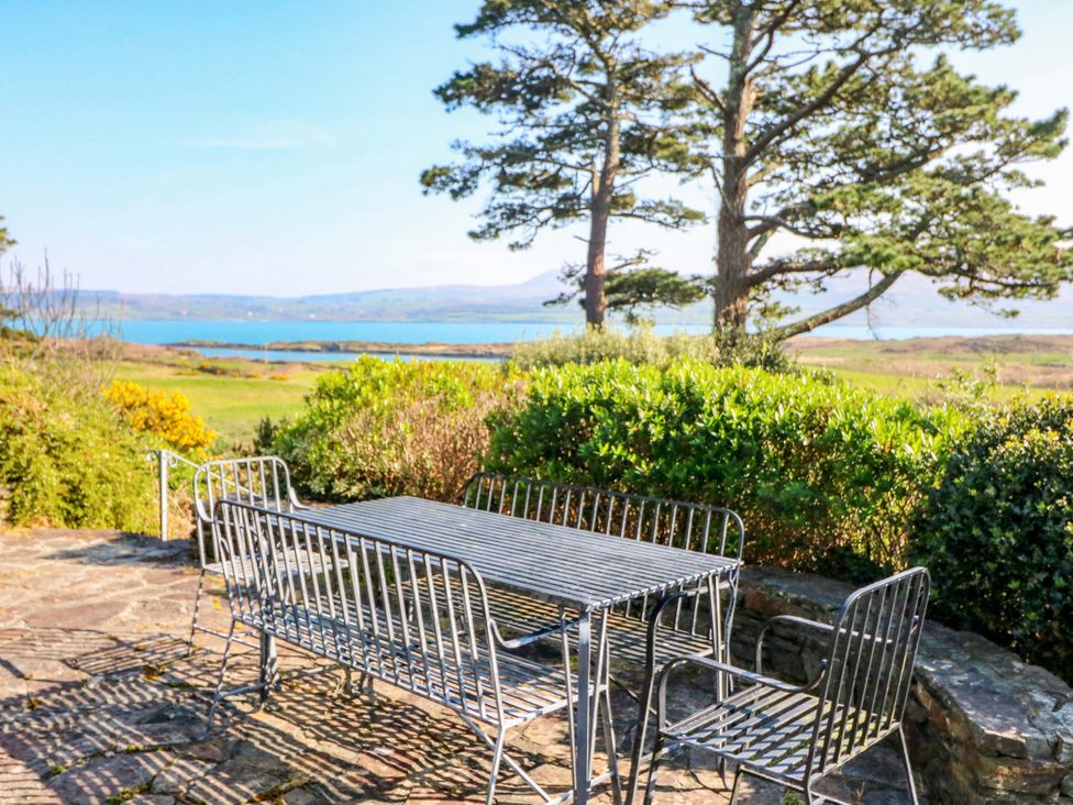 An outdoor seating area with a table and chairs overlooking water and hills at Whispering Pines in Durrus, County Cork