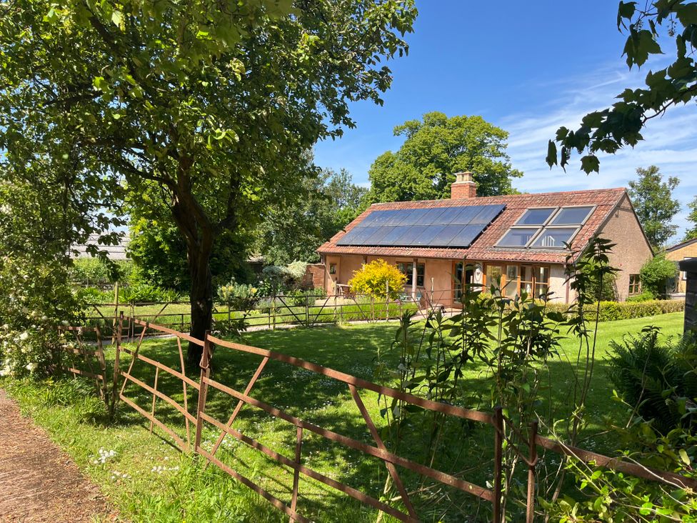 A house with solar panels on the roof behind a metal fence and trees at The Apple House in Spaxton near Nether Stowey