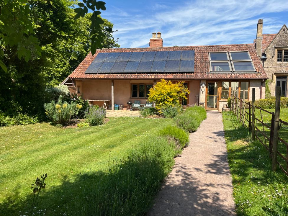 A pathway leading to a house with solar panels on the roof and a garden with bushes and grass at The Apple House in Spaxton near Nether Stowey