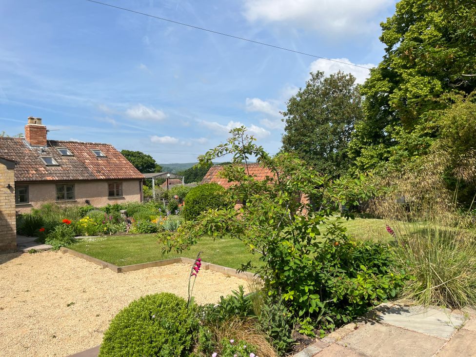 A garden with shrubs, flowers, lawn, and a house with a tiled roof at The Apple House in Spaxton near Nether Stowey
