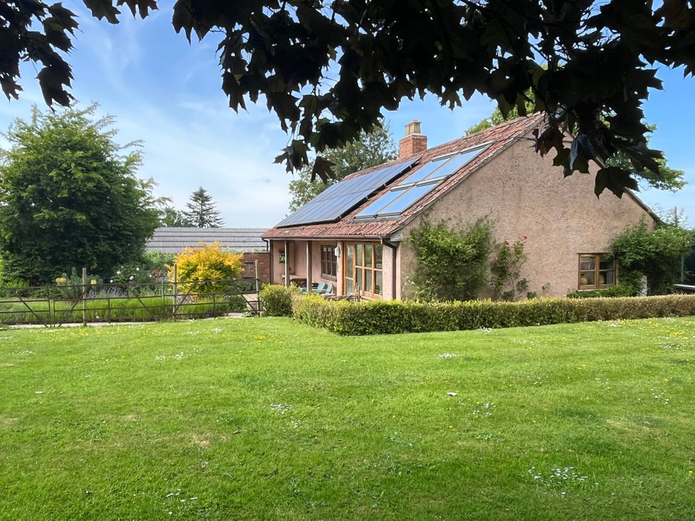 A single-story house with solar panels on the roof and a large green lawn in front at The Apple House in Spaxton near Nether Stowey