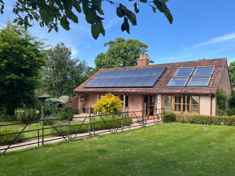 A house with solar panels on the roof surrounded by trees and grass at The Apple House in Spaxton near Nether Stowey