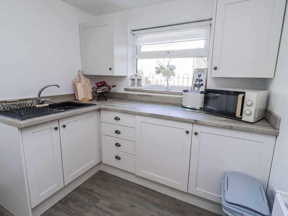 A kitchen with a sink, microwave and kitchen cabinets at Old Colliery Cottage in Shilbottle