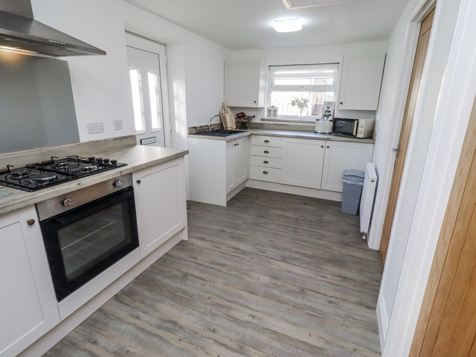 A kitchen with a gas stove and microwave at Old Colliery Cottage in Shilbottle