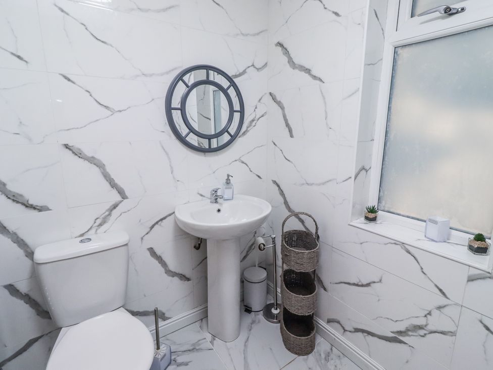 A bathroom with a sink, toilet, mirror, and window at Old Colliery Cottage in Shilbottle