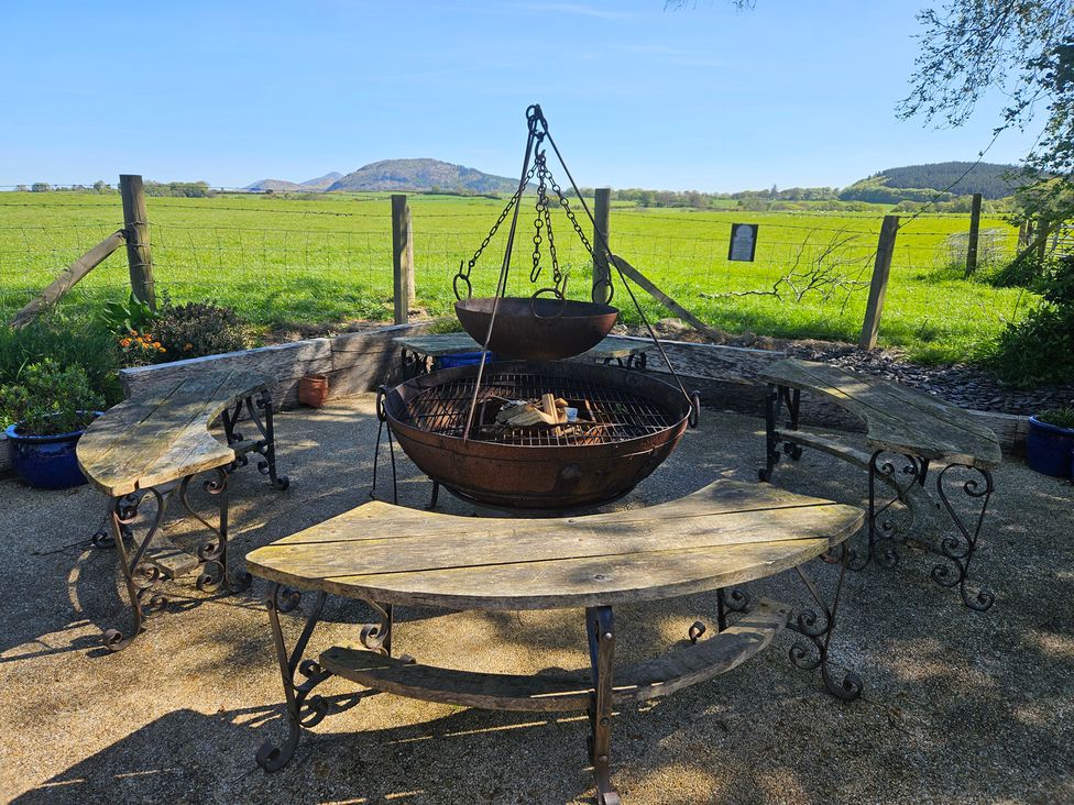 An outdoor seating area with a fire pit and wooden benches at The Keepers Lodge in Boduan near Nefyn