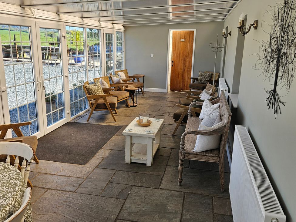 A conservatory with glass doors and wooden furniture at The Keepers Lodge in Boduan near Nefyn